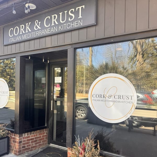 Exterior of Cork & Crust Italian Kitchen, featuring its sign and window decals.