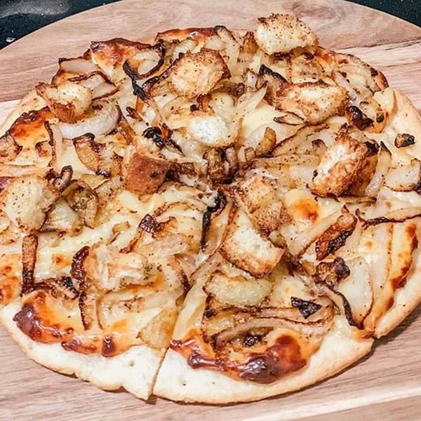 Close-up of a Cork & Crust Italian Kitchen pizza topped with caramelized onions, cheese, and croutons.