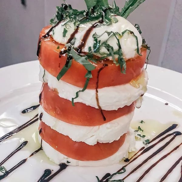 Stacked Caprese salad with fresh mozzarella, tomatoes, basil, and balsamic glaze on a white plate.