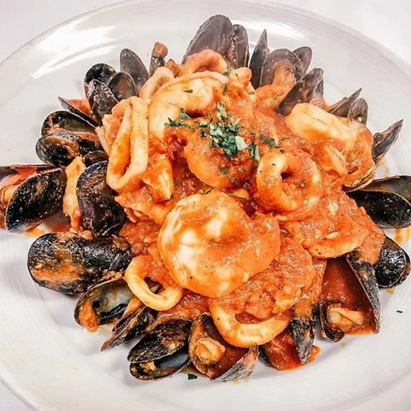 A white plate piled high with mussels, shrimp, and calamari in a rich red sauce.