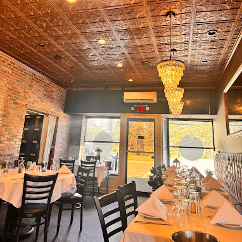 Cork & Crust Italian Kitchen dining room with set tables, brick walls, and ornate ceiling tiles.